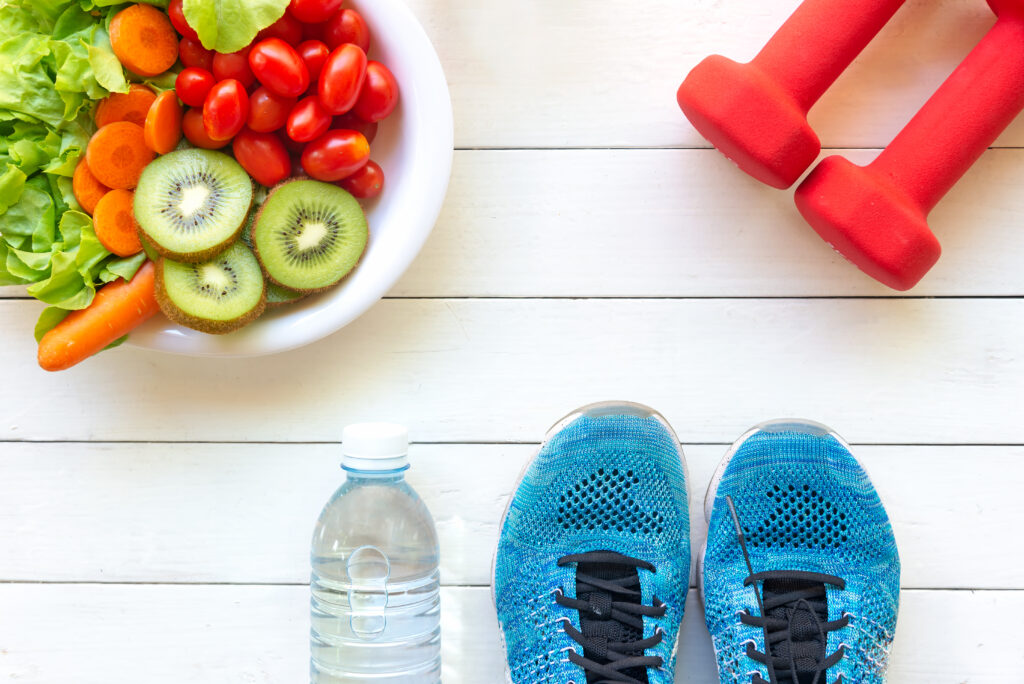 A bowl of fruit, set of dumbbells, bottle of water, and running shoes sitting on a table