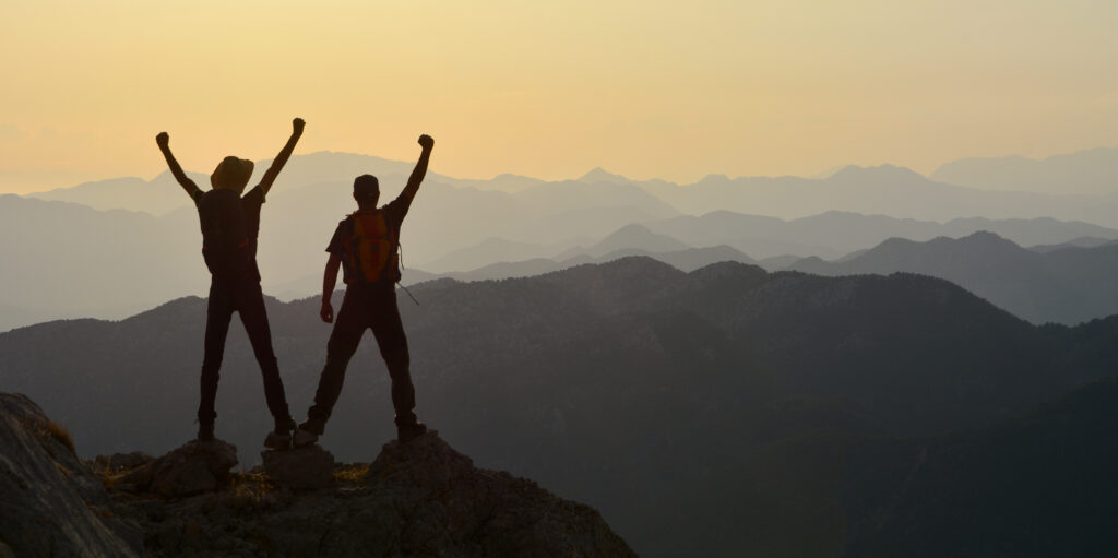 Two people standing on a mountain top with their hands in the air 