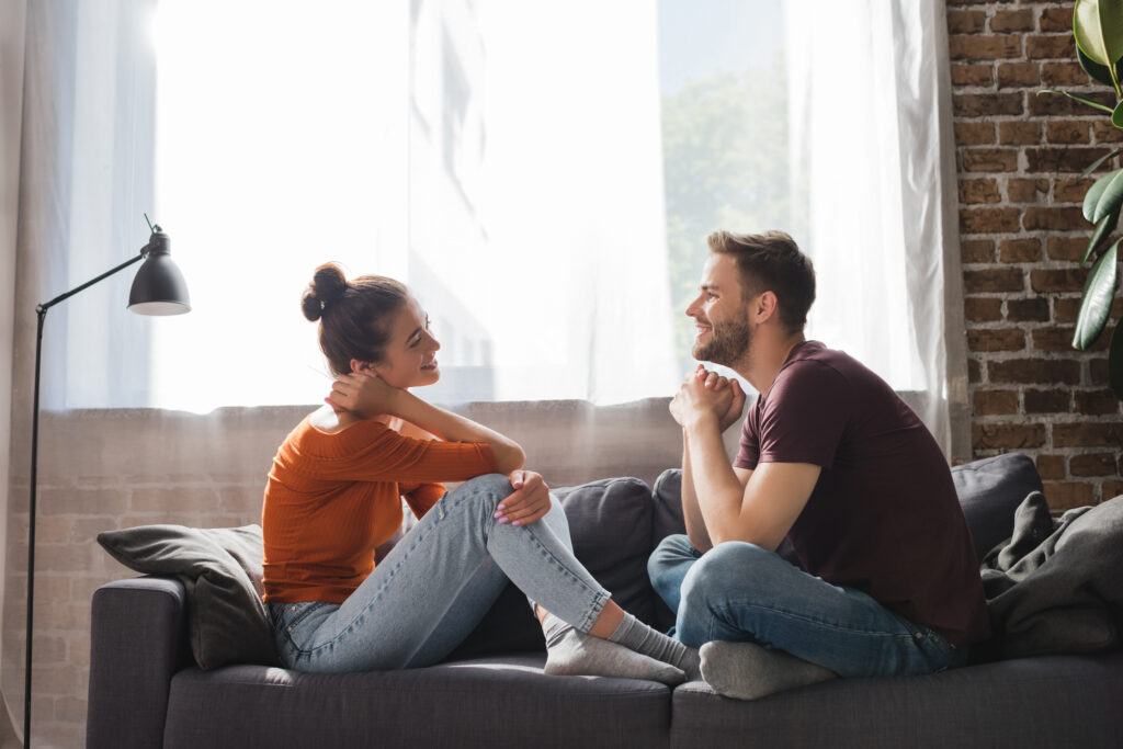 side view of young couple sitting on sofa and talking while looking at each other