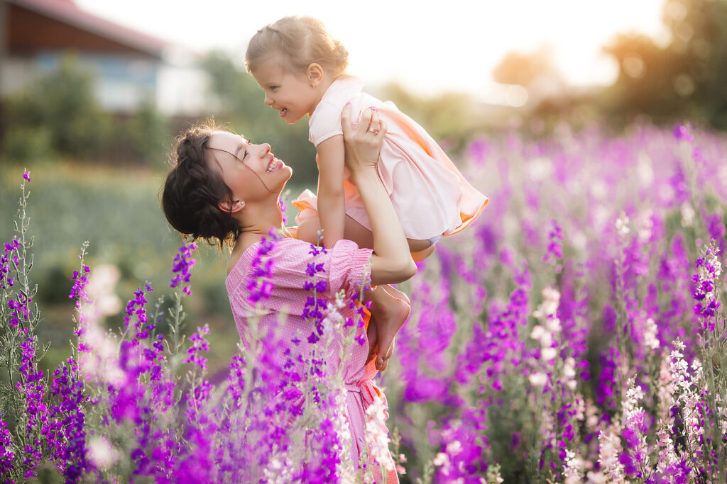 A woman standing in a field holding her daughter in the air