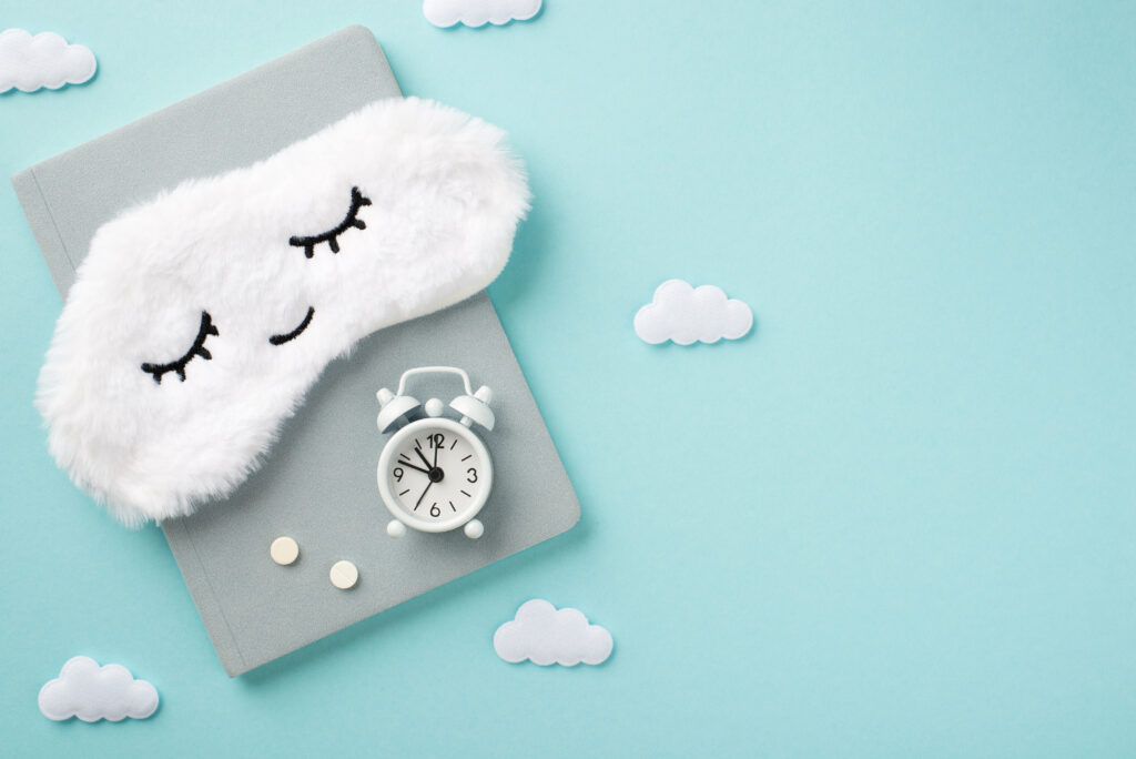 Top view photo of the tender white sleep mask on a grey diary with white small clock 