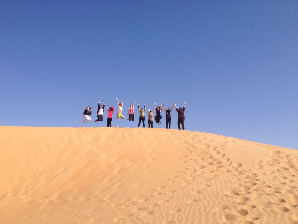 Ten people jumping in the air on top of a sand dune 