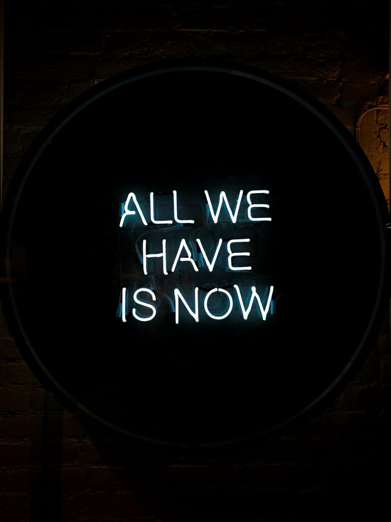 A white neon sign that reads ALL WE HAVE IS NOW 