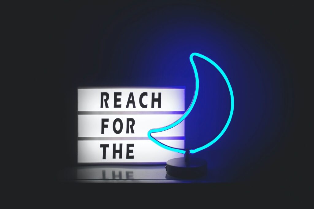 A neon sign that says REACH FOR THE MOON