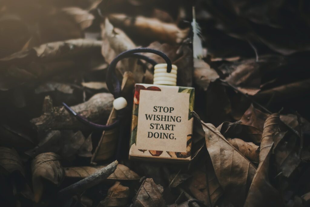 A small sign lying in a pile of leaves.  The sign says "Stop Wishing, Start Doing".