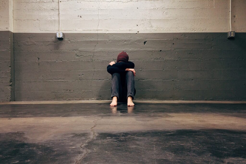 Someone sitting on a concrete floor with their head resting in their arms