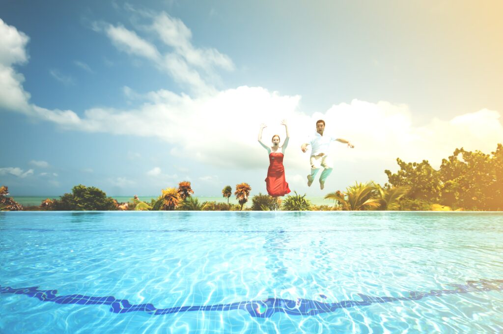 A man and woman jumping in a pool with their clothes on 