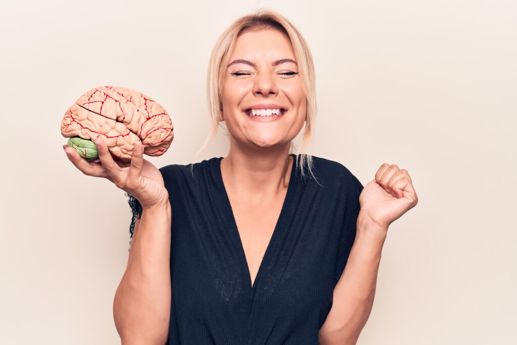 A woman smiling and holding a plastic model of a brain