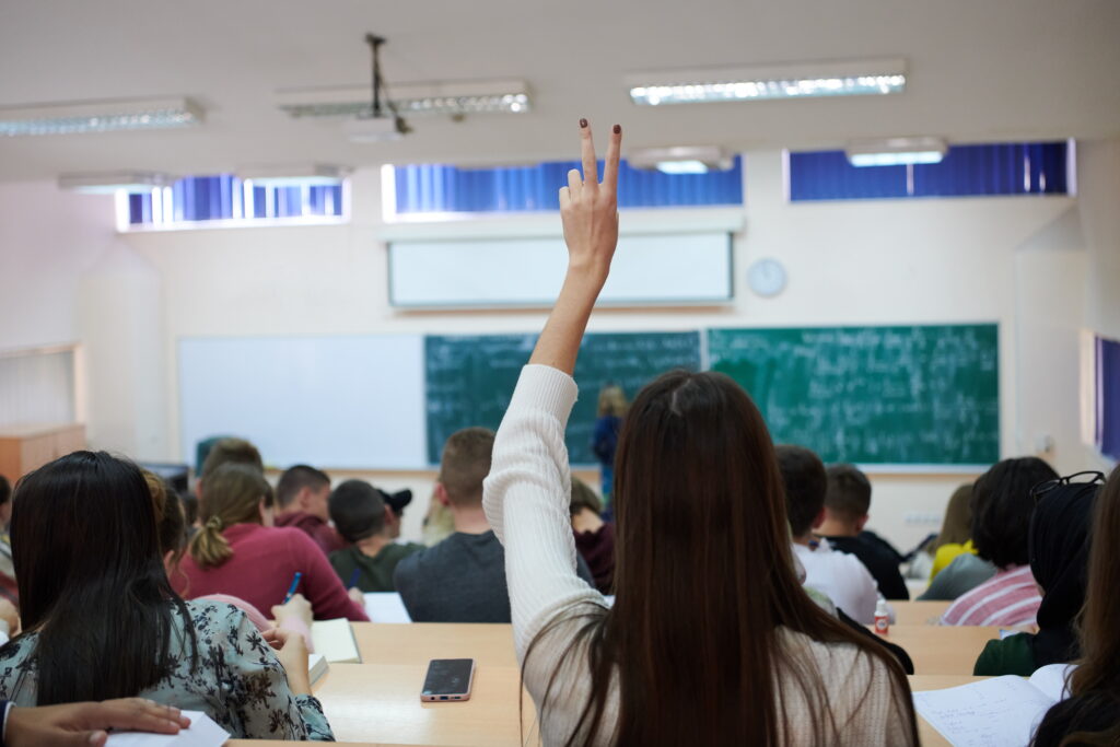 The rear view of a female sitting in class, raising her hand