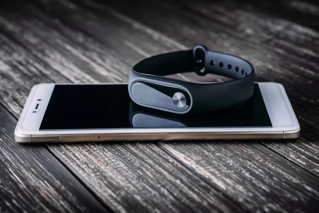 An iphone with a fitness tracking wrist band sitting on top of it