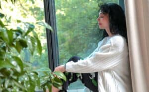 Woman sitting quietly by a window, reflecting — life coaching vs therapy in a calm, judgment-free space