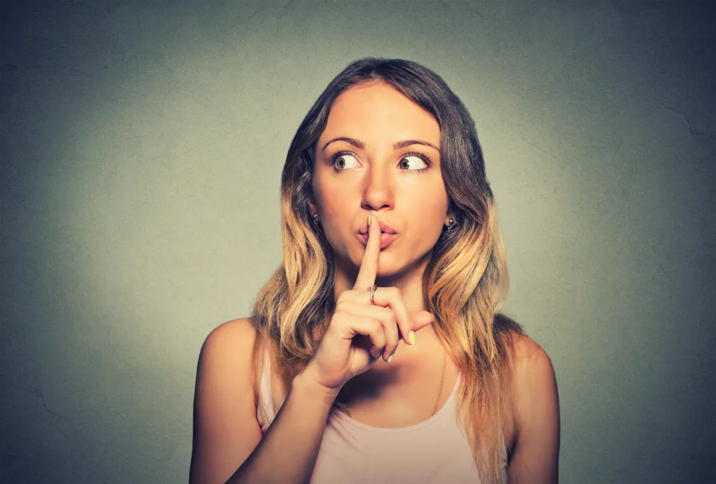 Closeup portrait young woman placing finger on lips asking shh, quiet, silence looking sideway isolated gray background. 