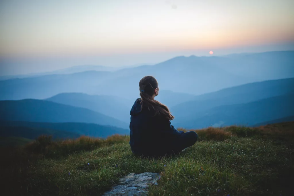 A person sitting on a hill, watching a sunrise
