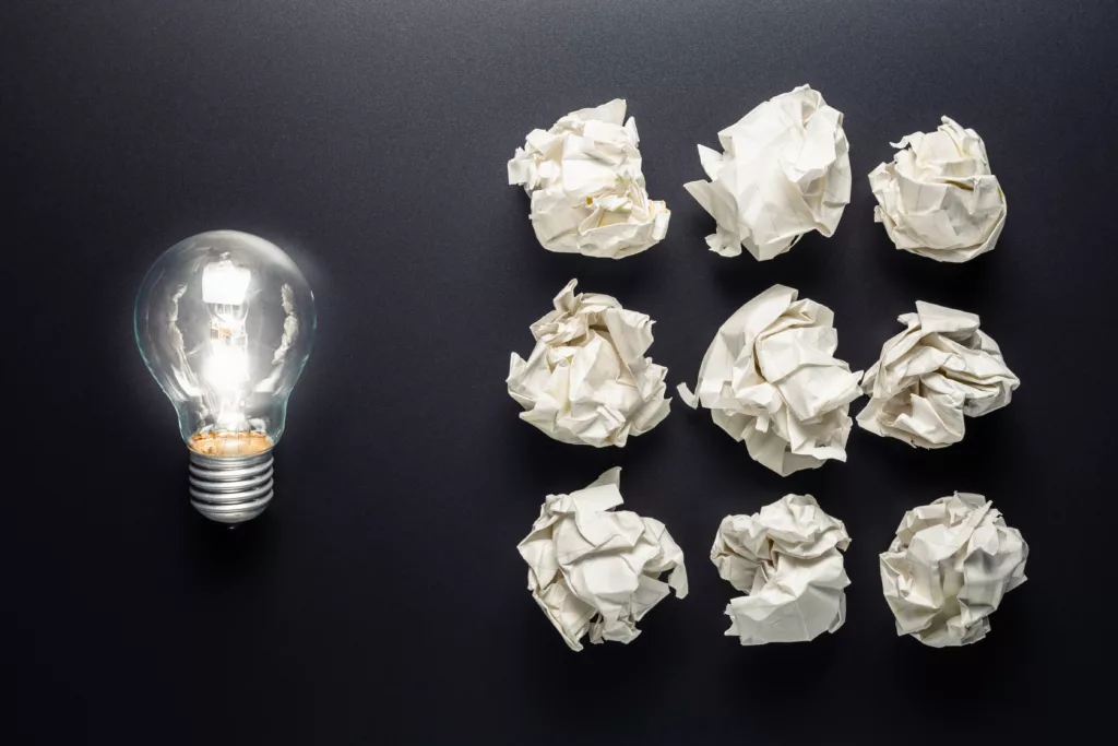 Glowing light bulb and group of crumpled paper balls, learn from mistakes