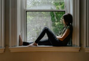 A woman sitting quietly by a window thinking about life coach or therapist